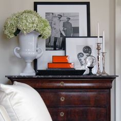 a white vase filled with flowers sitting on top of a wooden dresser next to pictures and candles