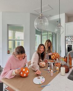 three women sitting at a kitchen table painting pumpkins