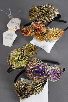 three different colored masks on top of each other with gold and purple feathers in them