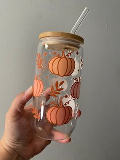 a hand holding a glass with pumpkins and leaves on it