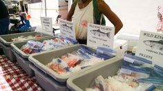 a woman standing next to bins filled with food at an outdoor vendor's booth