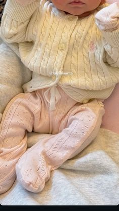 a baby wearing a hat and sweater laying on top of a bed