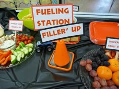 a table topped with lots of fruits and vegetables next to signs reading fueling station filler'up