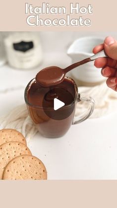 a person holding a spoon over a jar of chocolate next to crackers and cookies