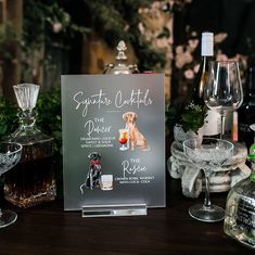 there is a sign on the table with wine glasses and bottles in front of it