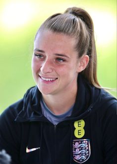 a woman smiling and wearing a black jacket with an england badge on it's chest