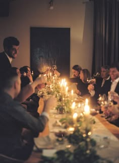 a group of people sitting around a dinner table with candles in front of their faces