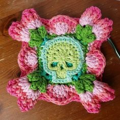 a crocheted flower with green leaves and pink petals on top of a wooden table