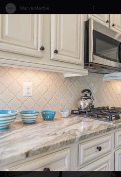 a kitchen with white cabinets and marble counter tops, blue bowls on the stove top