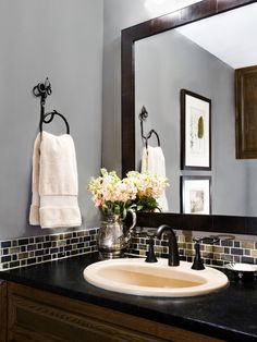 a bathroom sink sitting under a mirror next to a vase with flowers on top of it