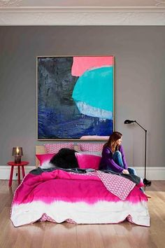 a woman sitting on top of a bed with pink and white comforter next to a painting