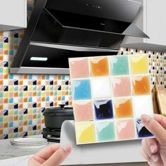 two hands holding up a square sticker in front of a stove top oven with colorful tiles on it