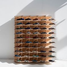 a wooden shelf filled with toy cars on top of white floor next to a wall