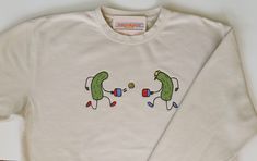 Independent Trading Co beige sweatshirt with two cartoon applique pickles playing pickleball. The design measures approximately 10x4 inches and is machine embroidered. Fun Hoodie Designs, Pickleball Painting, Pickleball Shirts Funny, Pickle Shirt, Pickleball Sweatshirt, Pickleball Outfit, Playing Pickleball, Quilt Size Chart, Beige Sweatshirt