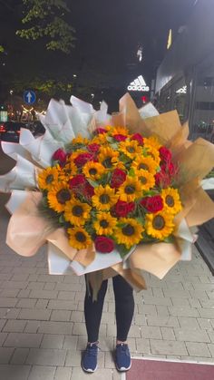 a person holding a bouquet of sunflowers and roses