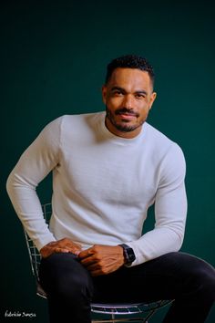 a man sitting on top of a chair wearing a white shirt and black pants with his hands in his pockets