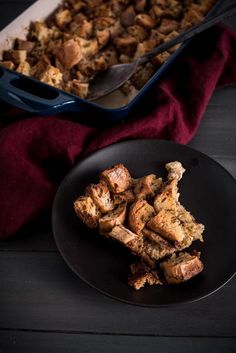 a black plate topped with pieces of bread next to a casserole dish filled with stuffing