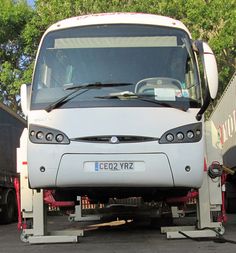 the front end of a white bus parked in a parking lot next to some trees