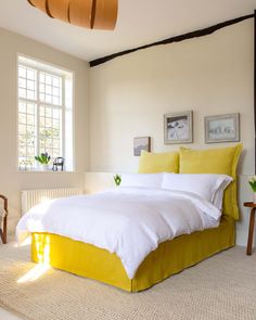 a bed with white and yellow linens in a bedroom next to a large window