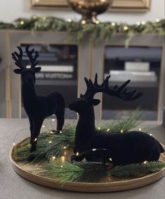 two black deer figurines sitting on top of a wooden tray covered in christmas lights