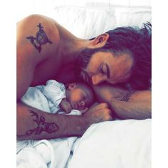 a man laying in bed next to a baby with tattoos on his arms and chest