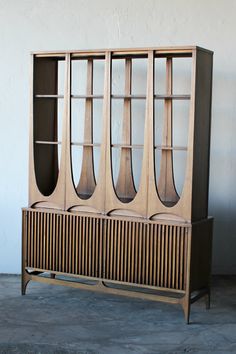 a wooden cabinet with four doors and three shelves on each side, against a white wall