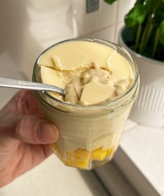 a person holding a spoon in a jar filled with pudding and butter on top of a counter