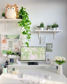 a white desk topped with a computer monitor next to a keyboard and mouse covered in plants