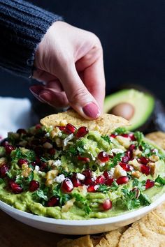 someone dipping guacamole into a bowl with tortilla chips on the side