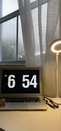 an open laptop computer sitting on top of a desk next to a lamp and window