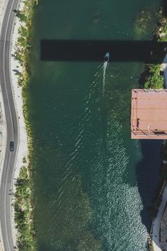 an aerial view of a boat traveling on the water next to a road and bridge