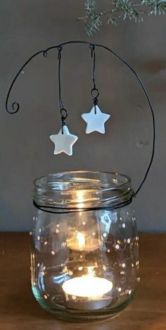 two white stars hanging from a wire in a mason jar filled with water and lit candles