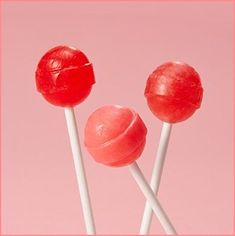 two red lollipops sitting on top of each other in front of a pink background