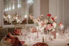 the table is set with pink and white flowers in vases, napkins, and wine glasses