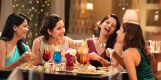 four women sitting at a table laughing and having drinks in a fancy restaurant with chandeliers hanging from the ceiling