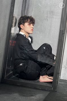 a young man sitting on the ground in front of a window wearing a suit and tie