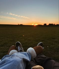 the person is laying down on the grass with their feet up in the air as the sun sets