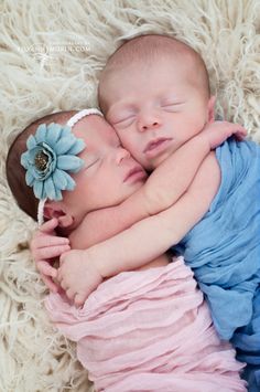 two newborn babies are cuddling together on a fluffy white blanket with a flower in their hair