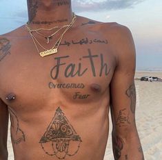 a man with tattoos on his chest standing in the sand