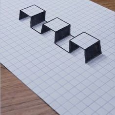 three black cubes sitting on top of a piece of paper with squares in the middle