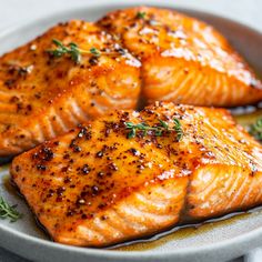 three salmon fillets on a plate with herbs