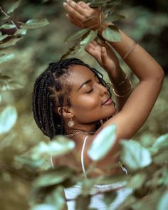 a woman with dreadlocks standing in front of some leaves and looking up at the sky