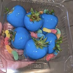 a plastic container filled with blue fruit covered in gummy bears and other candies