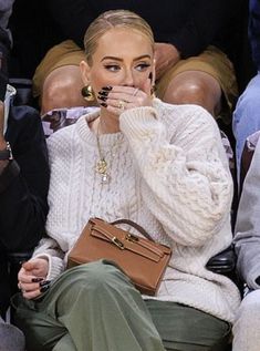 a woman sitting in front of a crowd holding her hand up to her mouth and looking at the camera