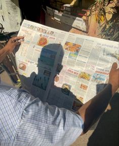 a man reading a newspaper with his shadow on the paper and holding it in his hand