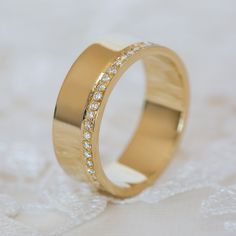 a gold wedding ring with small diamonds on it's side, sitting on a white surface