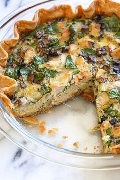 a quiche with spinach, cheese and other toppings on a glass plate