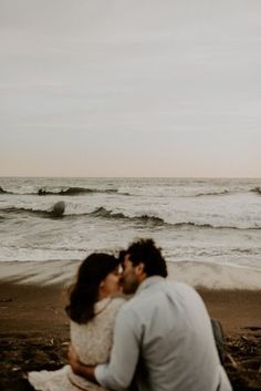 a man and woman kissing on the beach with waves in the backgroung