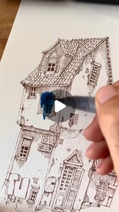 someone is drawing a house on paper with a marker and blue pen in their hand