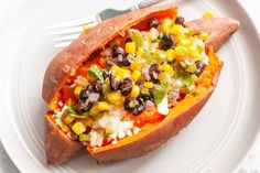 a white plate topped with a stuffed sweet potato filled with black beans, corn and feta cheese